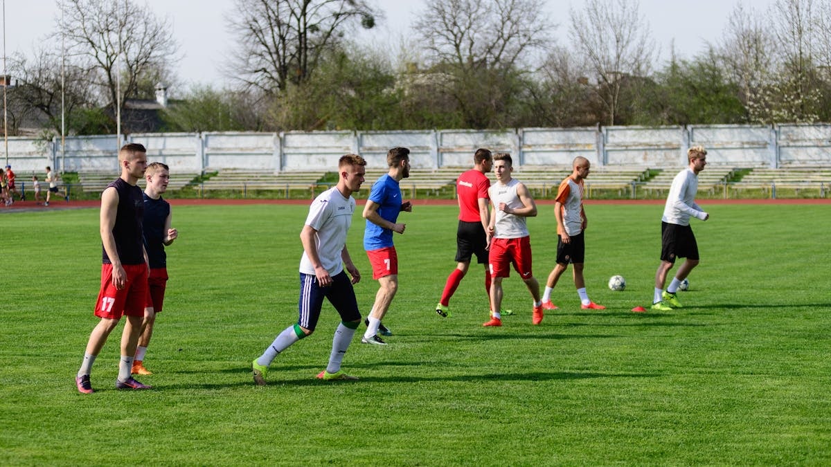 A group of young male athletes practicing soccer on an outdoor field on a sunny day.